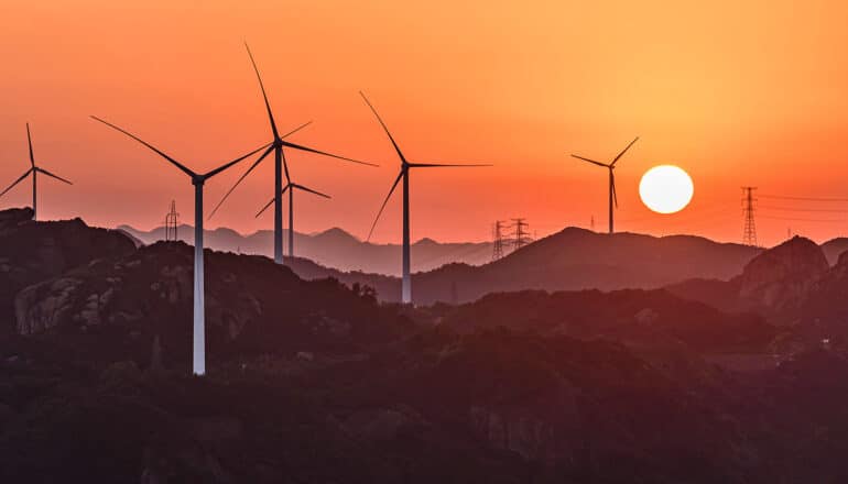 Wind turbines on a hill range at sunset.