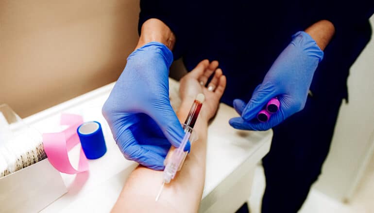 A health worker wearing blue gloves draws blood from a patient's arm.