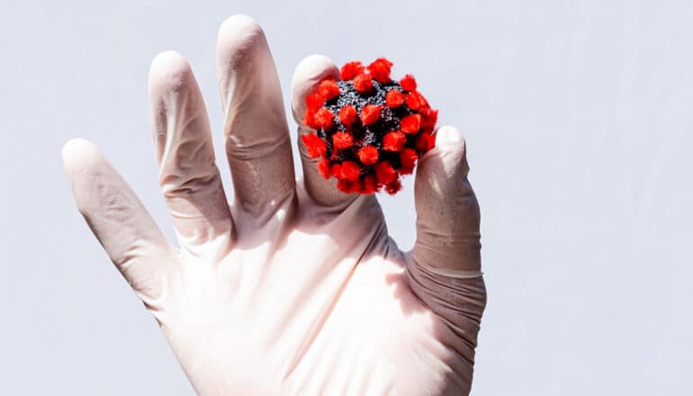 A person wearing a white glove holds up a model of the Covid virus.