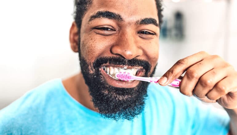 A man brushes his teeth while looking into the camera.