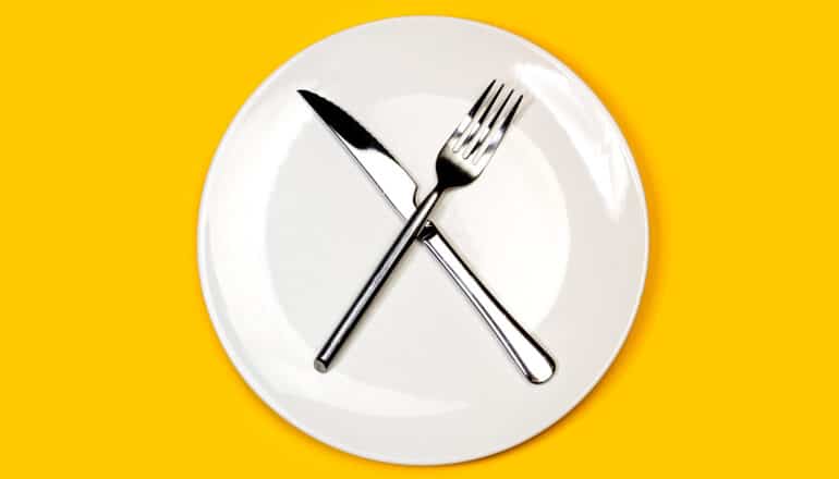 A fork and knife crossed in the shape of a "X" on a white plate on a yellow background.