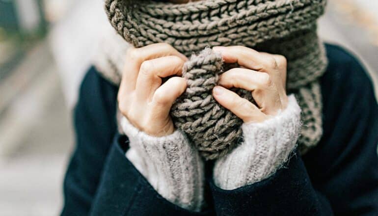 A woman holds a scarf over her face while walking outside.