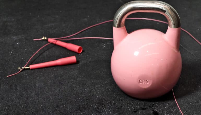 A pink kettlebell and pink jumprope on a black gym floor.