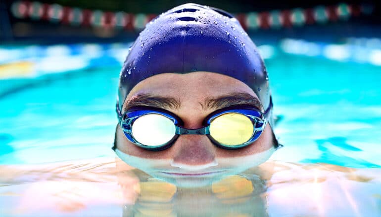 A person wearing a swim cap and goggles has their face halfway submerged in a swimming pool.