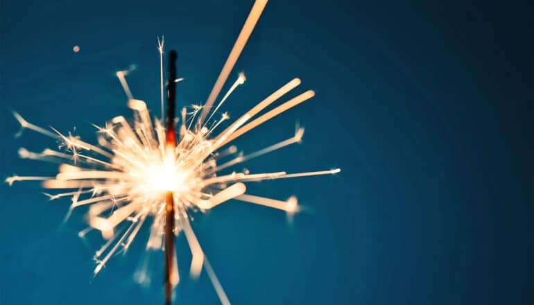 A sparkler burning and sparking against a dark blue background.