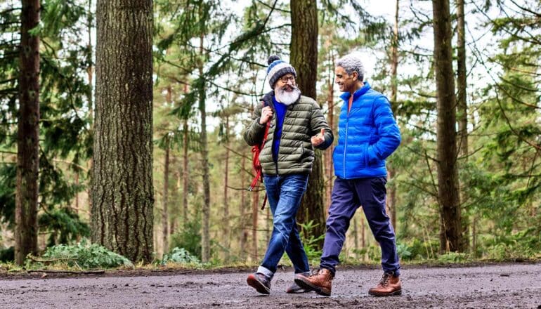 Two men walking on a trail through a forest.