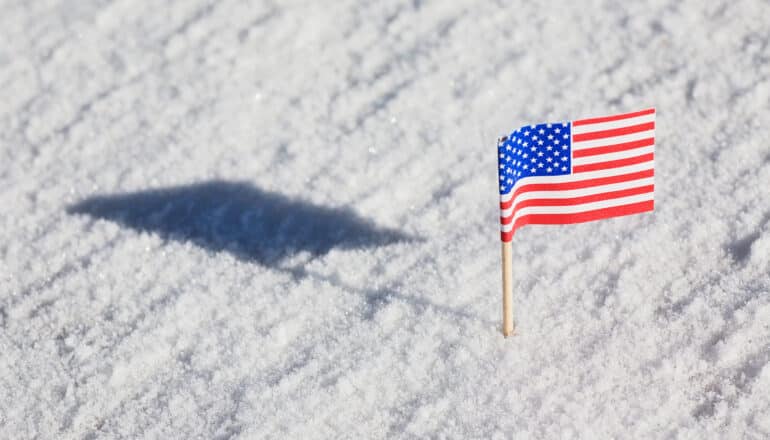 A tiny American flag on a toothpick stuck in snow.