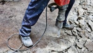 A construction worker uses a jackhammer to break up concrete.