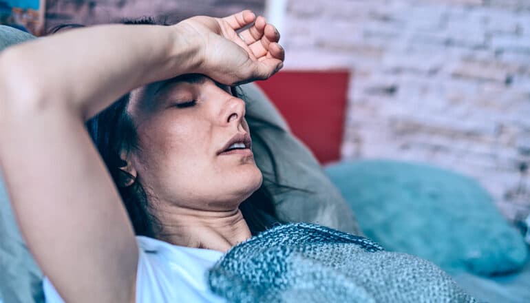 A woman sick in bed with her arm resting on her forehead.