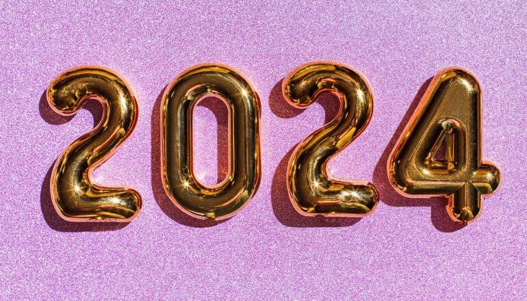 Gold balloons on a purple, glittery surface read "2024."