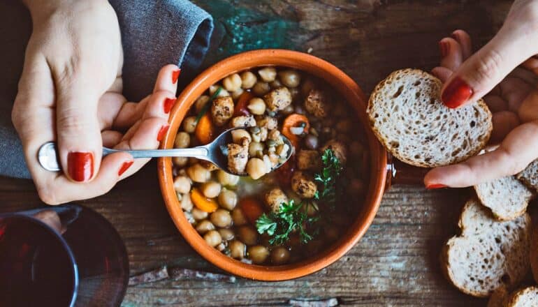 A woman eats a bean-based soup and some bread at a wooden table.