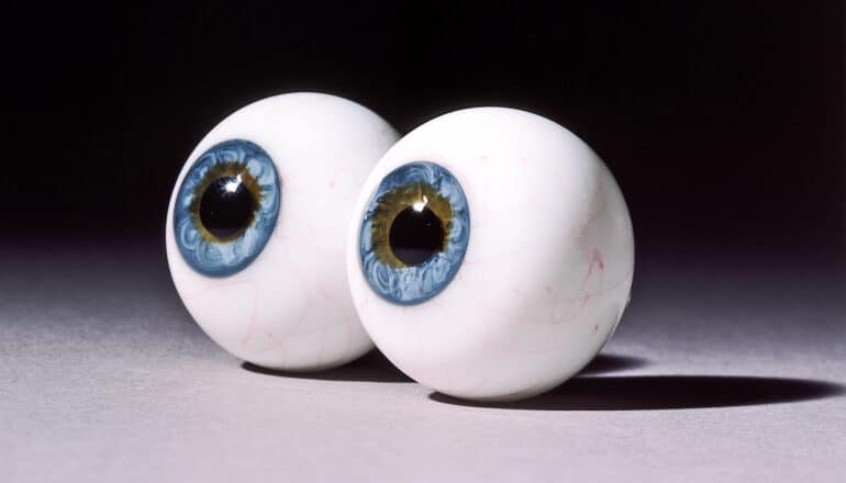 Two human eyeball models sitting on a white surface with a black background.