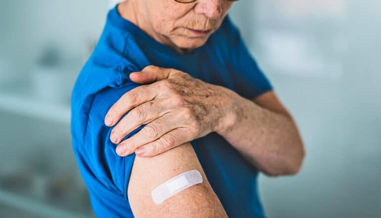 A man looks down at a bandage on his arm covering a vaccine injection site.