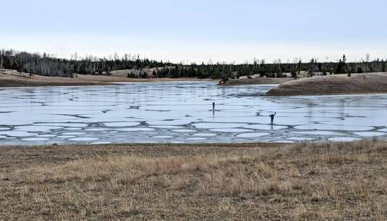 Two researchers stand on a frozen lake.