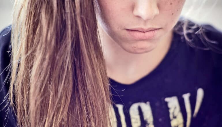 A young woman looks downward with a sad expression.