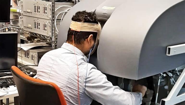 A person with electrodes attached to their head operates a surgery robot.