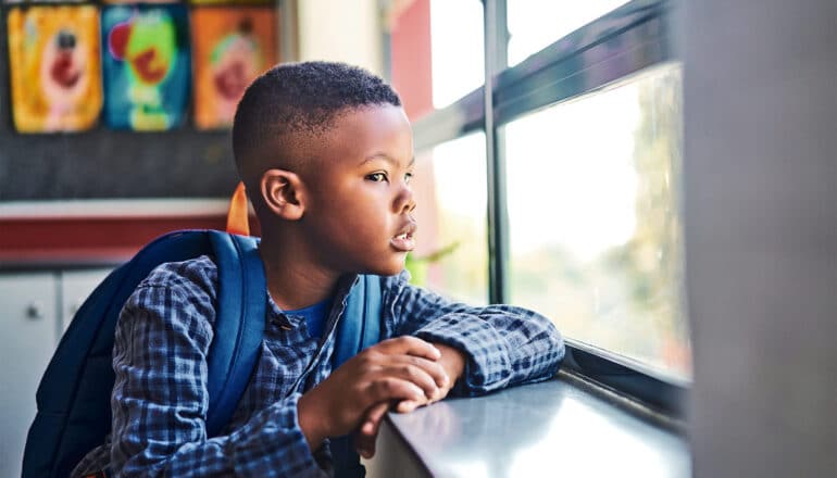 A young Black boy looks out the window at his school.