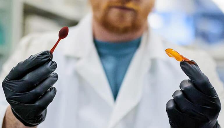 In one hand, the researcher holds plastic that's been shaped into a spoon and in the other a blobby, twisted shape of the same material.