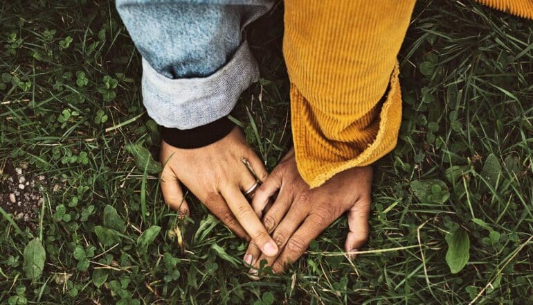 A couple touches hands while sitting on green grass.