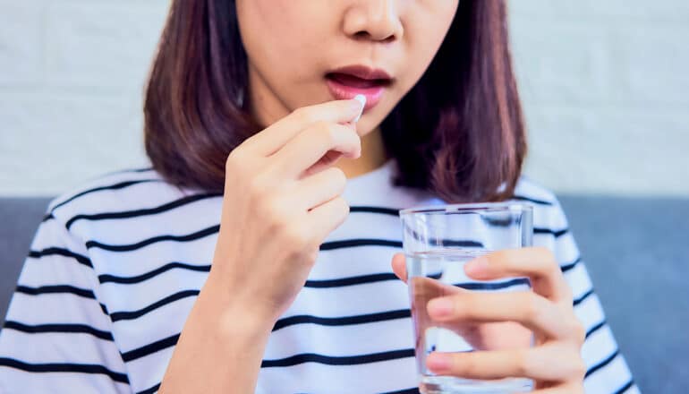 A young woman takes a white pill with a glass of water.