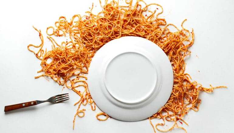 An overturned plate with spaghetti splattered under it on a white surface.