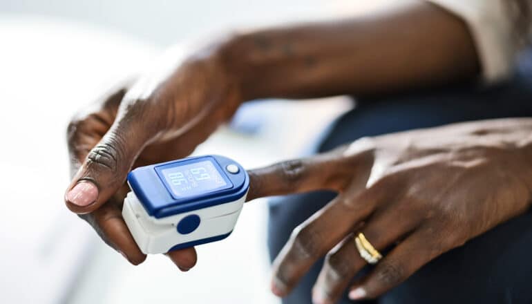 A person uses a pulse oximeter device on their left index finger.