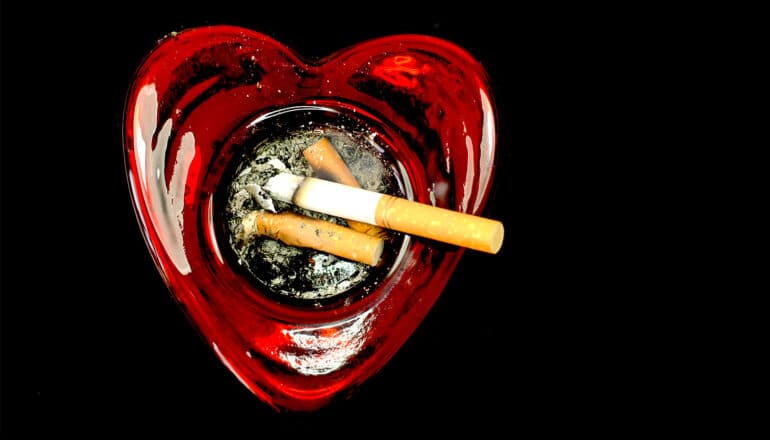 A heart-shaped ashtray with a few cigarette butts in it.