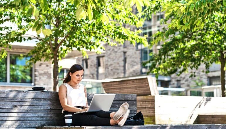 A woman works on her laptop while sitting outside in a park.