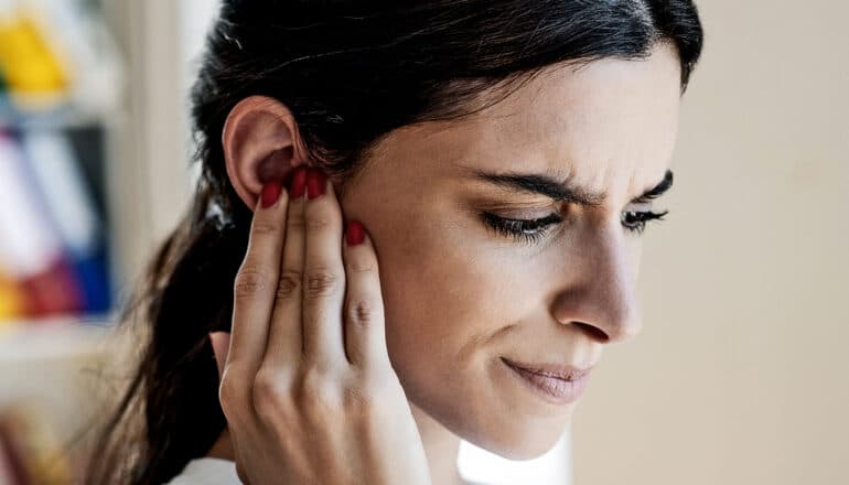 A woman grimaces and touches her ear.