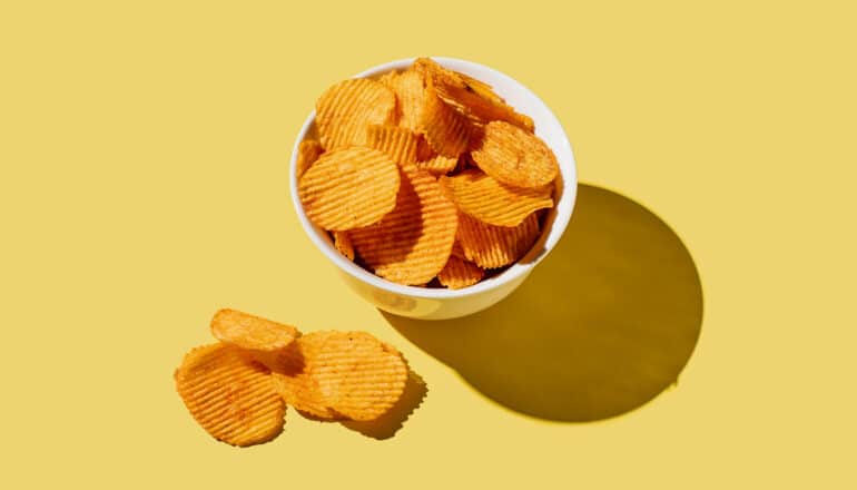 A bowl of potato chips on a yellow background.