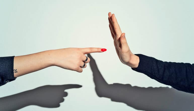 One person points a finger at another, who is holding up their hand in a "stop" gesture.