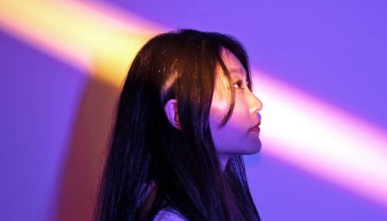 A shaft of light hits a young woman's face as she stands in profile.