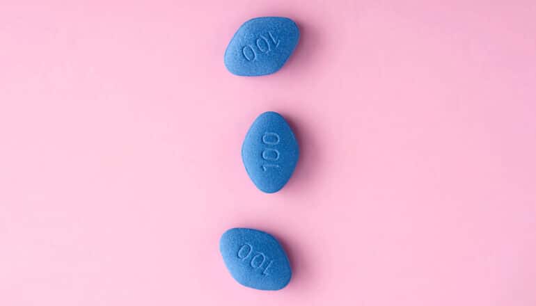 Three blue viagra pills on a pink background.