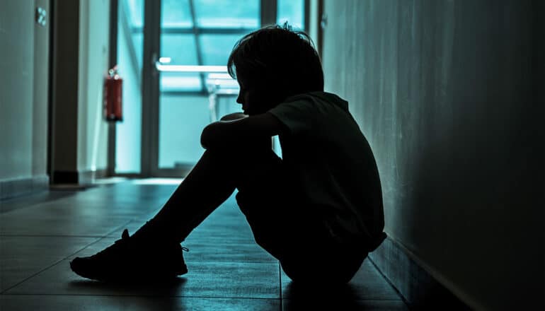 A young boy sits in a dark apartment building hallway.