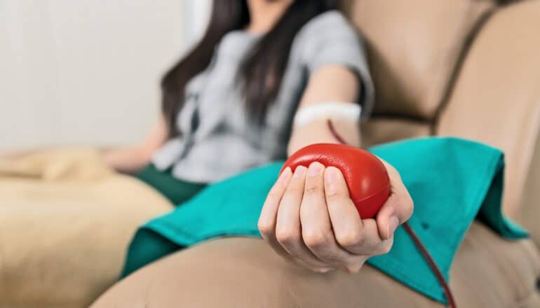 A person donating blood sits in a chair and squeezes a red stress ball.