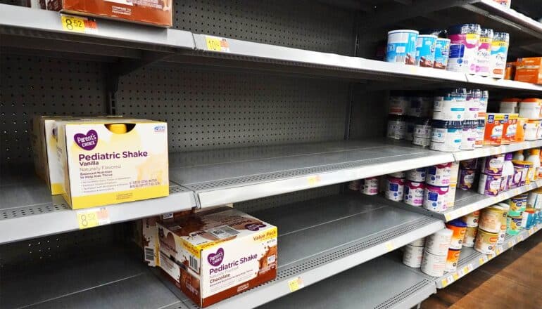 A supermarket shelf with very little baby formula left stocked.