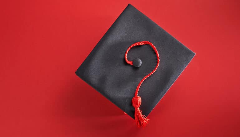 A mortar board from graduation with the red tassel shaped into a question mark.