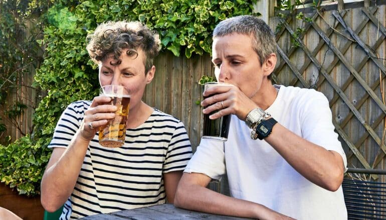 A couple sits in a backyard while sipping beer.