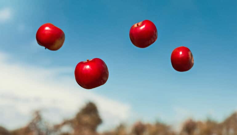 Four red apples fall through the air.