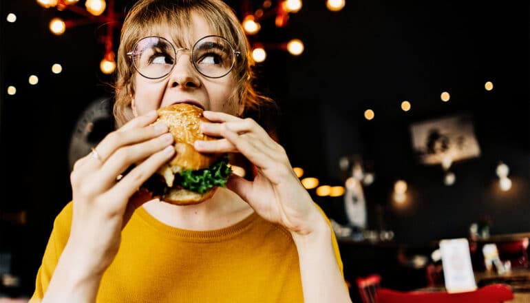 A woman takes a big bite of a hamburger.