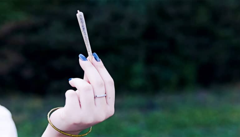 A young woman holds a joint in her hand.