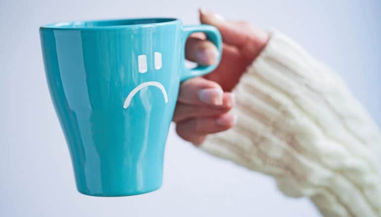 A person holds a coffee mug with a frowning face on it.