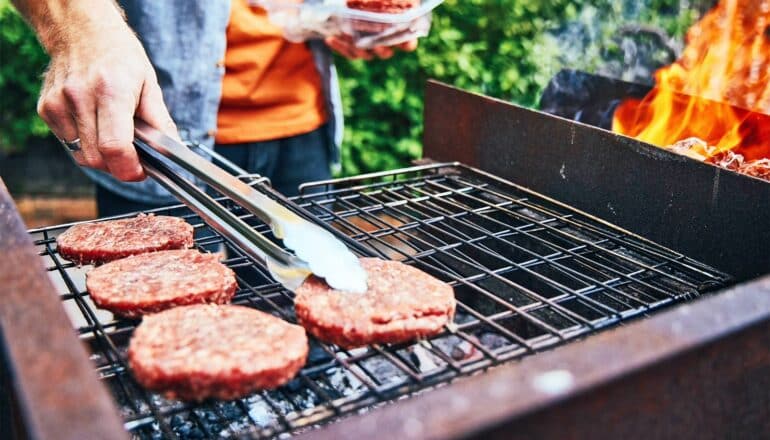 A man cooks burgers on a grill outside.