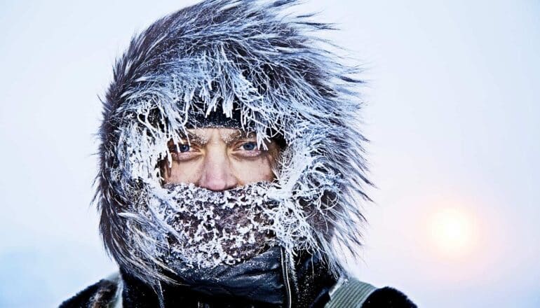 A man wearing a coat and scarf has snow and ice covering his hood.