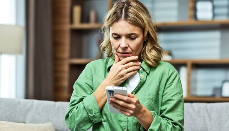 A woman looks worried as she reads something on her phone.