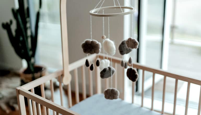 An empty crib with a mobile of rainclouds above it.