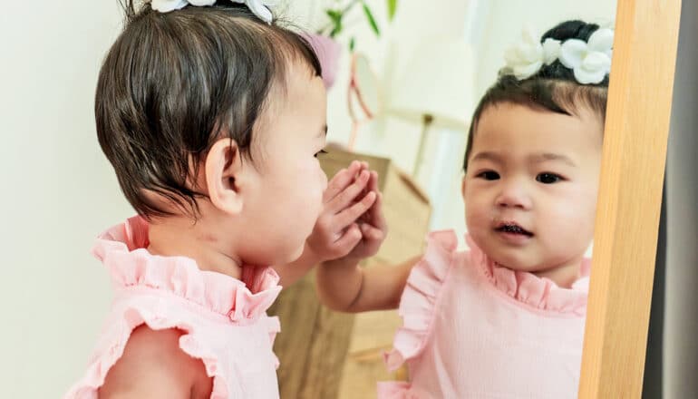 A baby girl touches a mirror while looking at her own reflection.