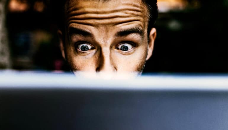 A man looks down at a laptop screen in shock.