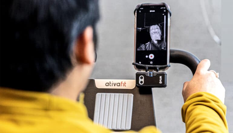 A researcher rides an exercise bike while a camera attached to a smartphone watches his face.