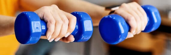 A woman holds two small blue weights in front of herself.